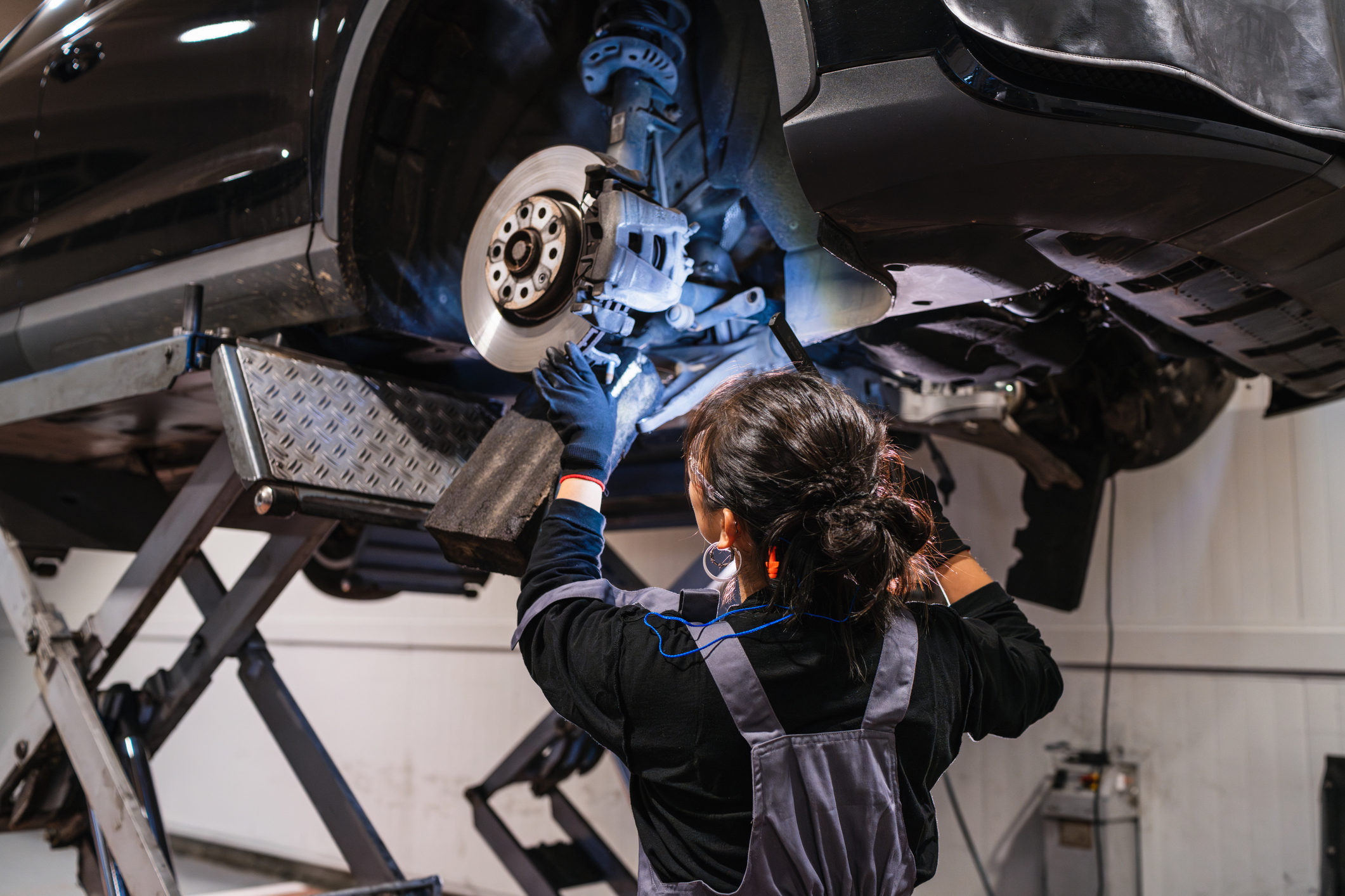 Technician servicing a brake rotor and caliper on a lifted vehicle