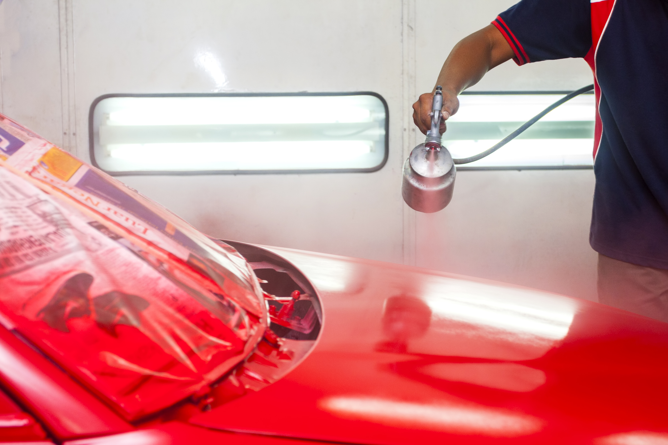Technician spray-painting a vehicle hood in the paint booth