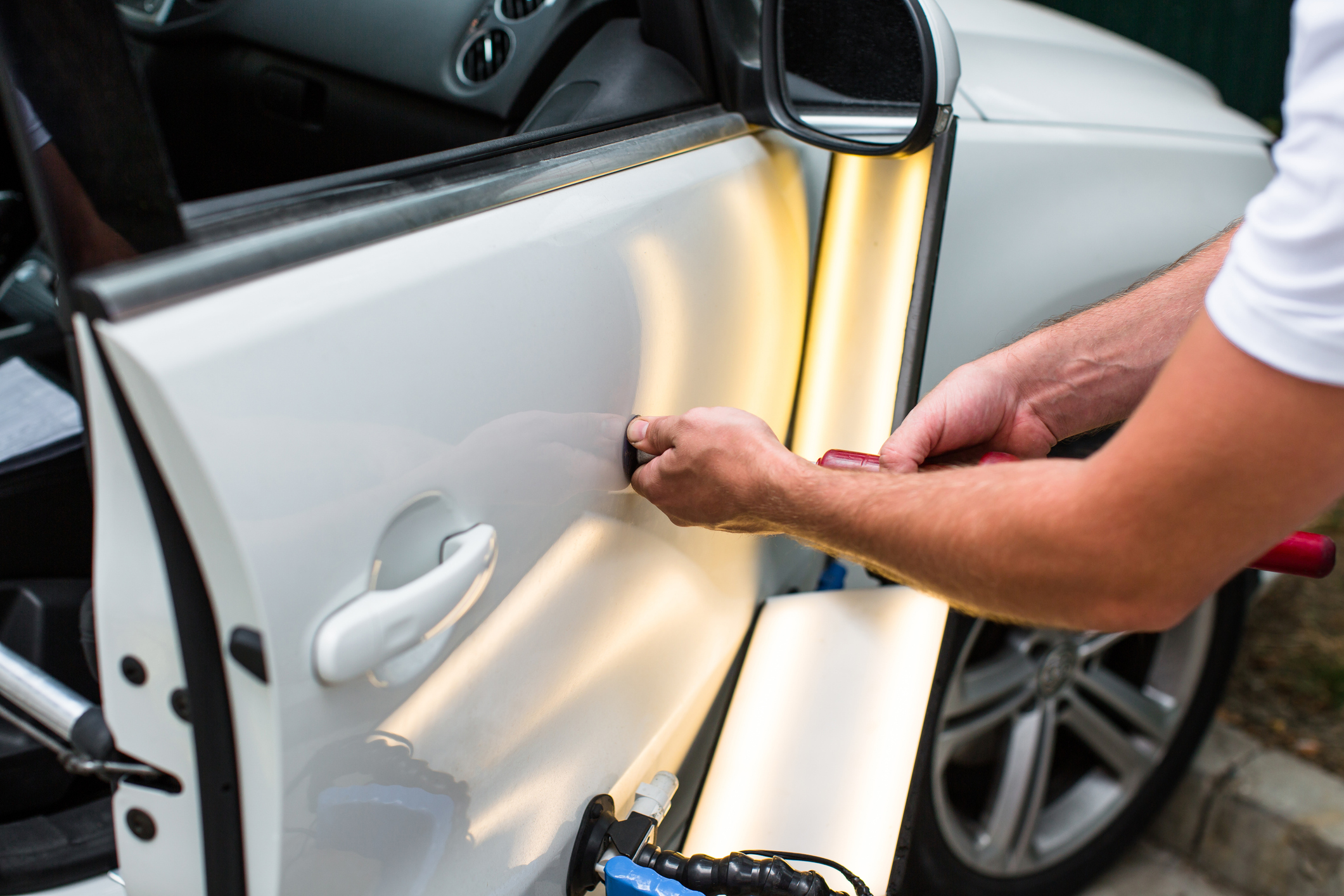 Technician using PDR rods and a reflection board to massage a dent from behind a door panel